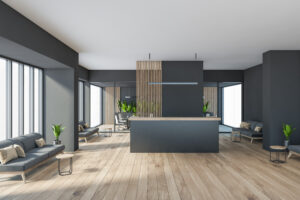 Dark modern minimalist office room interior with cozy couches, wooden parquet floor, panoramic window, reception desk, computer, glass partition.